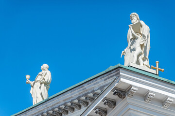 Fototapeta na wymiar Helsinki, Finland - July 19, 2022: Matthew the Evangelist carrying writing instruments on SE corner of pediment with John the Apostle to his left against blue sky