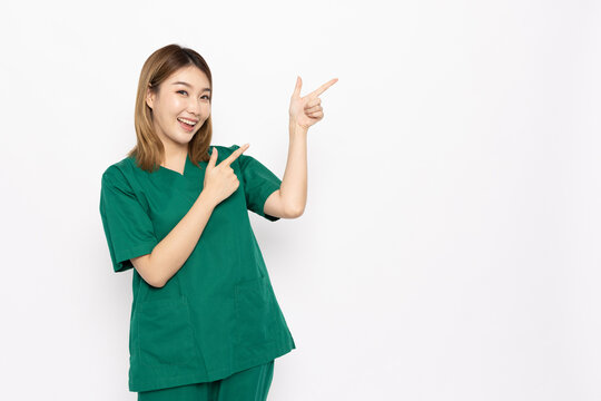 Young Asian Woman Wearing Green Nurses Scrubs Points To The Right Isolated On White Background