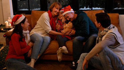 Happy diverse daughter and family joins grandparents by the couch to hug during Christmas in their...