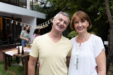 Naklejka premium Happy senior caucasian couple smile while there is an outdoor party behind them with a table of food