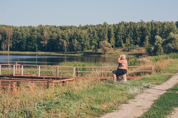 Old watchman sitting on high riverbank against forest landscape