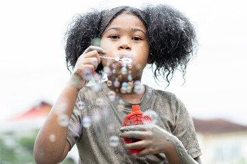 African American child girl playing wet mud puddle and blowing soap bubbles outdoor