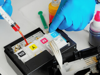 Printer maintenance. Master fills inkjet printer with ink or syringe paint. Hands with gloves...