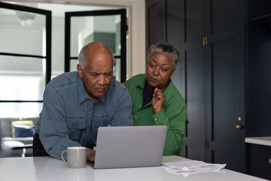 Worried senior couple at home looking at bills and personal finances using a laptop