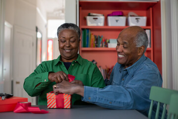 Happy senior couple wrapping Christmas presents at home together