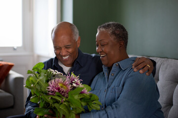 Senior African American husband giving bouquet of flowers to wife