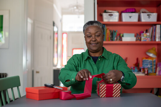 Happy african american senior female wrapping Christmas presents at home