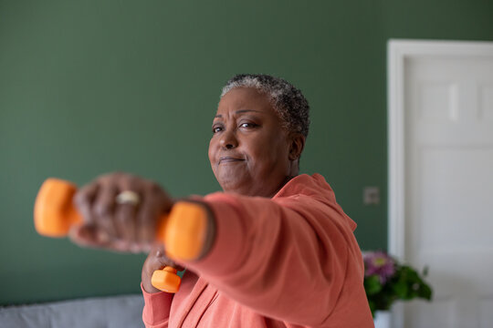 Senior African American female exercising at home with dumbbells 
