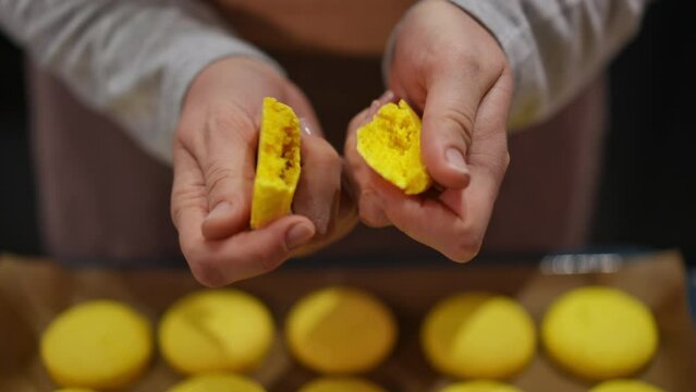 Close-up female hands breaking yellow delicious french macaroon cookie in slow motion. Unrecognizable Caucasian baker showing tasty pastry indoors