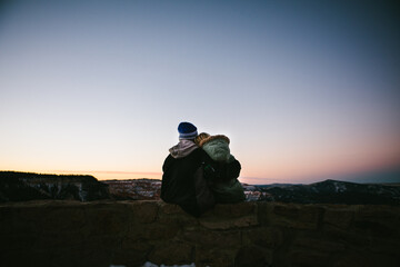 Brother and sister overlook snowy canyon in winter coats at sunset