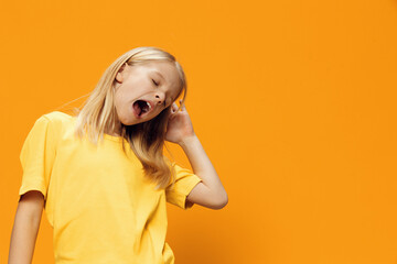 a cute sleepy school-age girl stands on a yellow background and yawns with her mouth wide open