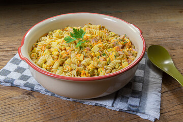 Travessa com deliciosa salada de macarrão e diversos legumes e vegetais, sobre toalha xadrez e fundo de mesa rústico.