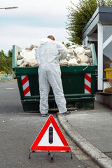 Construction worker stands in front of container with construction waste and removes iron bars