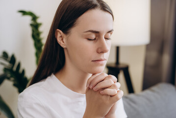 Cute girl praying sincerely with folded arms and making wish, asking with hopeful imploring...