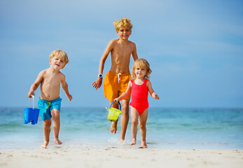 Three happy kids walk on the sand beach plying with toy buckets