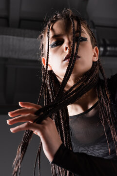 low angle view of stylish woman with braided dreadlocks looking at camera on grey background.