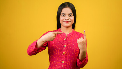 Young Indian girl showing finger after voting, cheerful girl isolated over yellow background