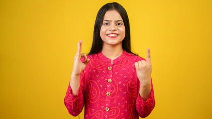 Young Indian girl showing finger after voting, cheerful girl isolated over yellow background