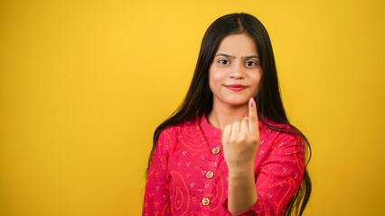 Young Indian girl showing finger after voting, cheerful girl isolated over yellow background