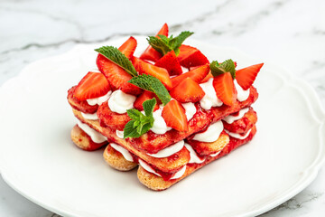 Tiramisu. Homemade tiramisu cake with fresh strawberry, mascarpone and mint. Tiramisu portion on plate on light background. Delicious no bake tiramisu