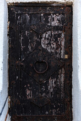 Very textured wooden door with black peeling paint, with metal handles. Vertical orientation.