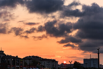Fototapeta na wymiar Orange sunset with sun disk, clouds, roofs of buildings.