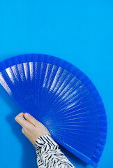 Woman's hand with blue fan on blue background