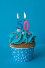 Birthday cupcake with with candles 50 fifty on a blue background. Cake with blue cream. Festive dessert and congratulations.
