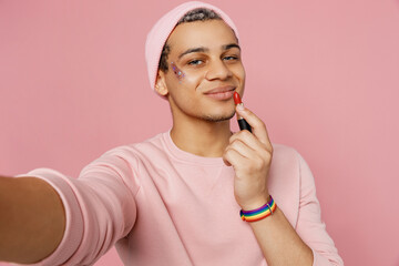 Close up young gay man wear sweatshirt hat do selfie shot pov on mobile cell phone use red lipstick isolated on plain pastel light pink color background studio portrait. Lifestyle lgbtq pride concept.