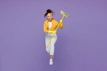 Full body young excited fun happy housekeeper woman wear yellow shirt tidy up jump high hold broom...
