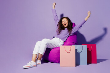 Full body fun excited happy young woman in pullover sit in chair near paper package bags after...