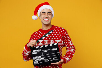 Merry young man wear red knitted christmas sweater Santa hat posing holding classic black film...