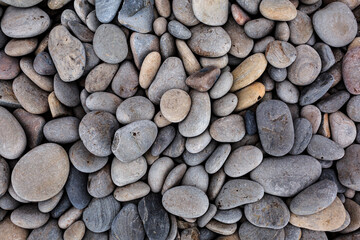 Many multi-colored stones of different oval and round shapes on the ocean, texture background of stones.
