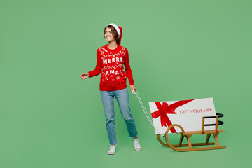 Full body merry fun young woman wear xmas sweater Santa hat posing carry store gift certificate...