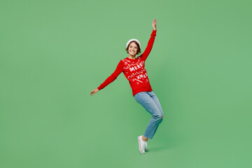 Fototapeta premium Full body merry young woman wear xmas sweater Santa hat posing leaning back stand on toes with outstretched hands dance isolated on plain pastel green background. Happy New Year 2023 holiday concept.