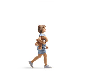 Full length profile shot of a little girl walking and carrying a teddy bear