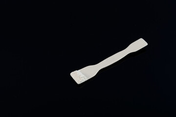 Titanium dioxide on laboratory spatula, TiO2 on dark surface. White chemical powder. Food additive...