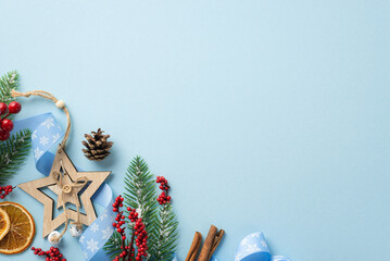 Christmas decor concept. Top view photo of fir branches wooden star ornament pine cone mistletoe berries curly ribbon dried orange slices and cinnamon on isolated pastel blue background with copyspace