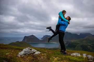 man holding his girlfriend in his arms, romantic photo of couple on top of a mountain overlooking the lofoten islands panorama, norway, couple hiking in the norwegian fjords - obrazy, fototapety, plakaty