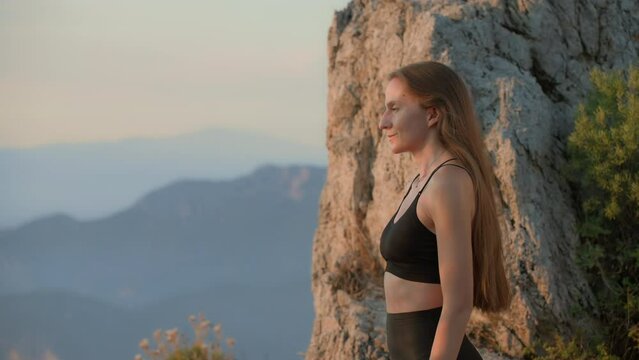 Side view Young woman with long brunette hair takes deep breath and opens eyes, looking into the distance. Close-up portrait. View from the viewpoint of the mountain. Sunset light Sports Lifestyle