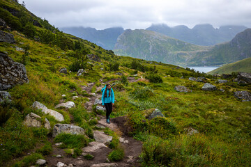 girl with a backpack hiking to the famous kvalvika beach on lofoten islands, norway; hiking in the norwegian fjords, rugged landscape of northern norway - obrazy, fototapety, plakaty