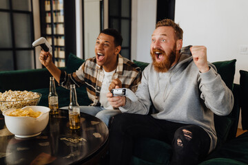 Two excited men gesturing as winners while playing video games in living room