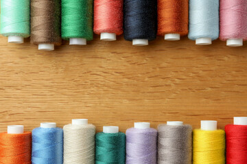 Many colorful sewing threads on wooden table, flat lay. Space for text
