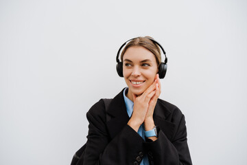 Young woman in headphones smiling while standing over white wall