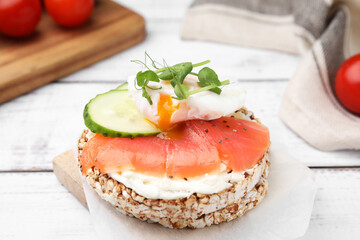 Crunchy buckwheat cakes with salmon, poached egg and cucumber slices on white wooden table