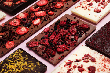 Different chocolate bars with freeze dried fruits on pink background