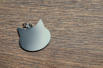Silver pet tag in shape of cat on wooden table, top view. Space for text