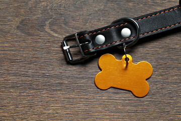 Leather dog collar with yellow tag in shape of bone on wooden table, flat lay. Space for text