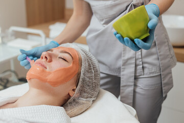 Cosmetic jelly mask, facial skincare. Cosmetologist applies alginate mask with spatula on face