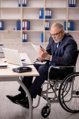 Old male employee in wheel-chair sitting at workplace